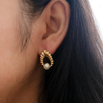 A person wears a vintage-style CAELLIA gold earring featuring a textured hoop and a pearl drop.