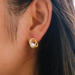 A person wearing a gold Camellia flower stud earring featuring a central freshwater pearl.
