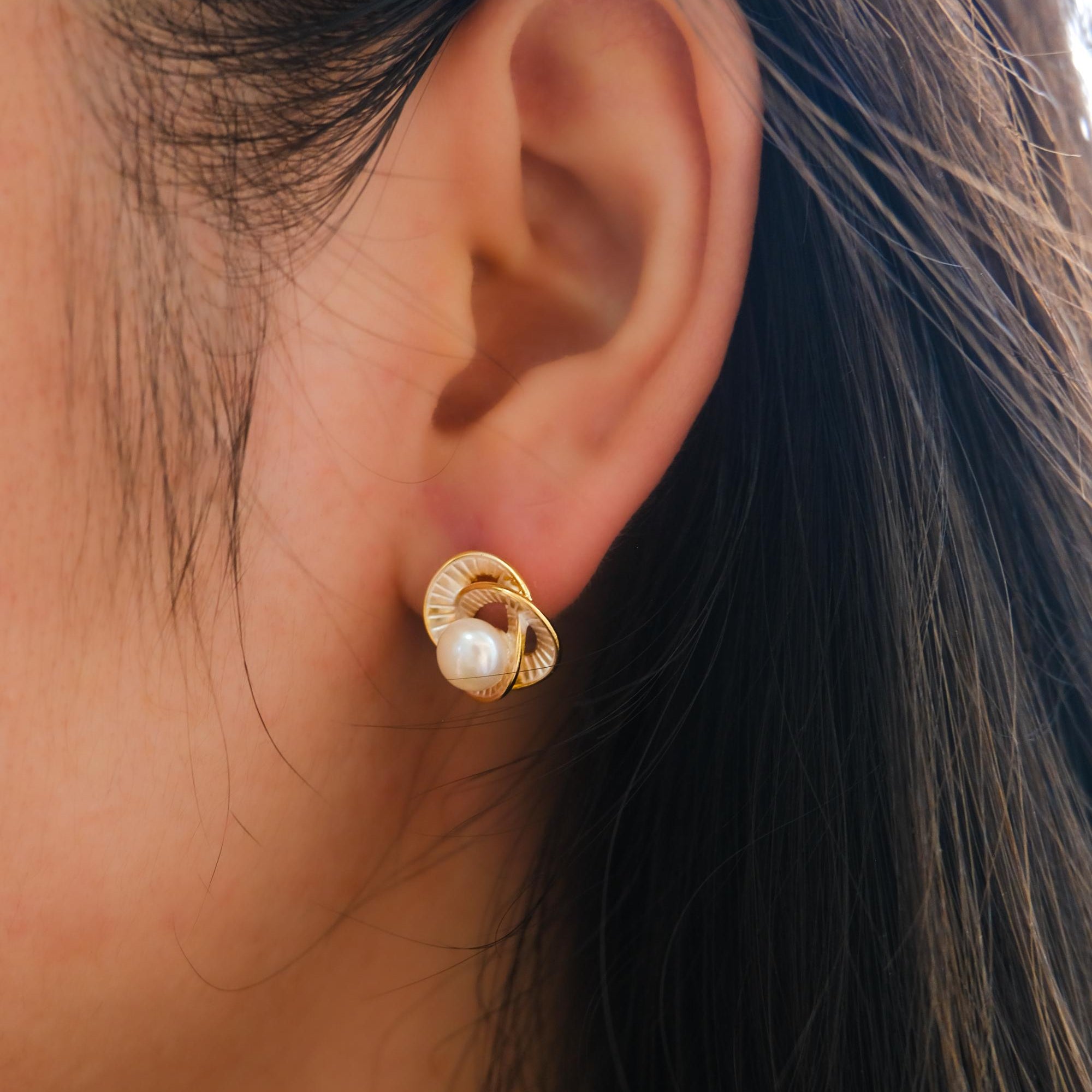 A person wearing a gold Camellia flower stud earring featuring a central freshwater pearl.