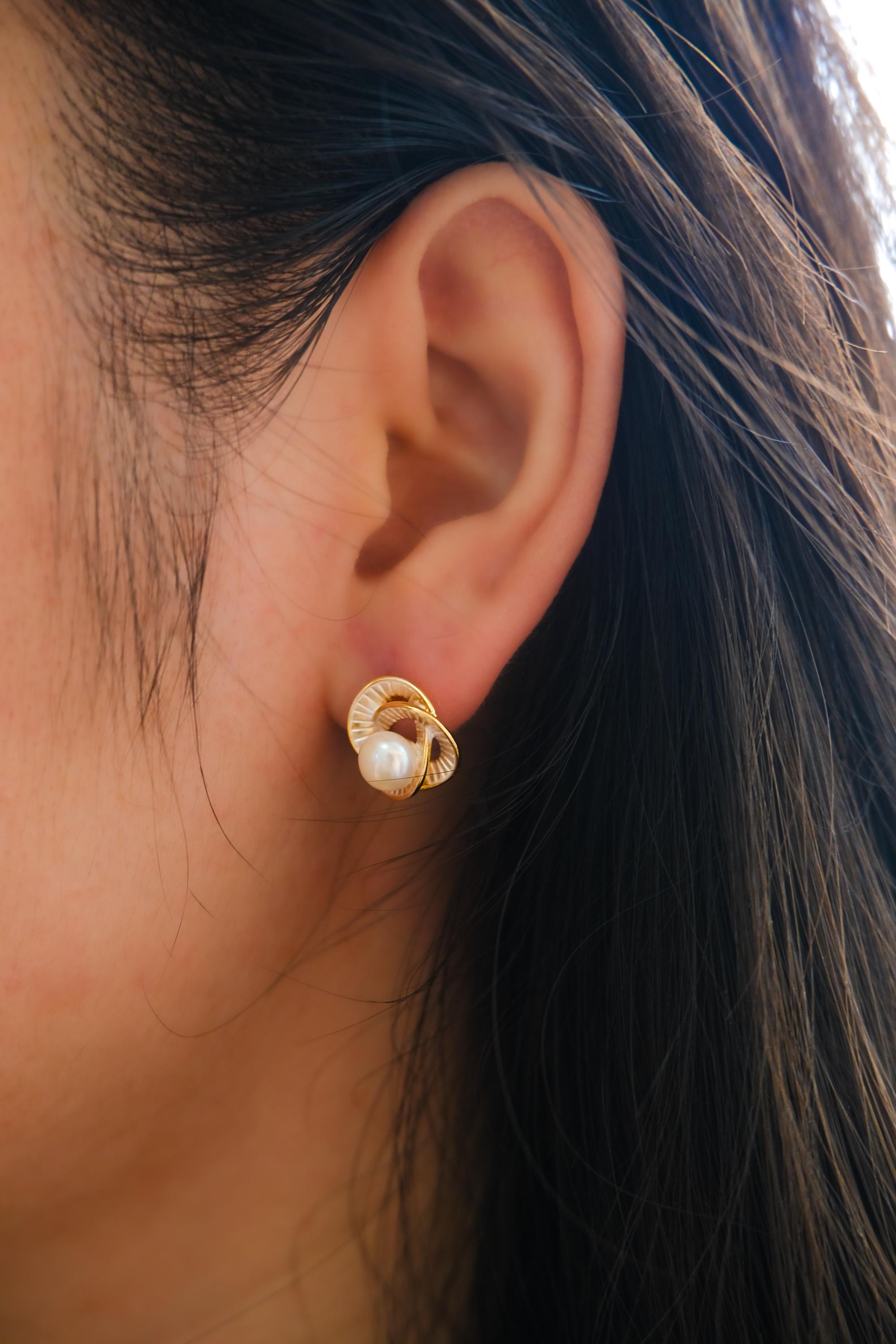A person wearing a gold Camellia flower stud earring featuring a central freshwater pearl.
