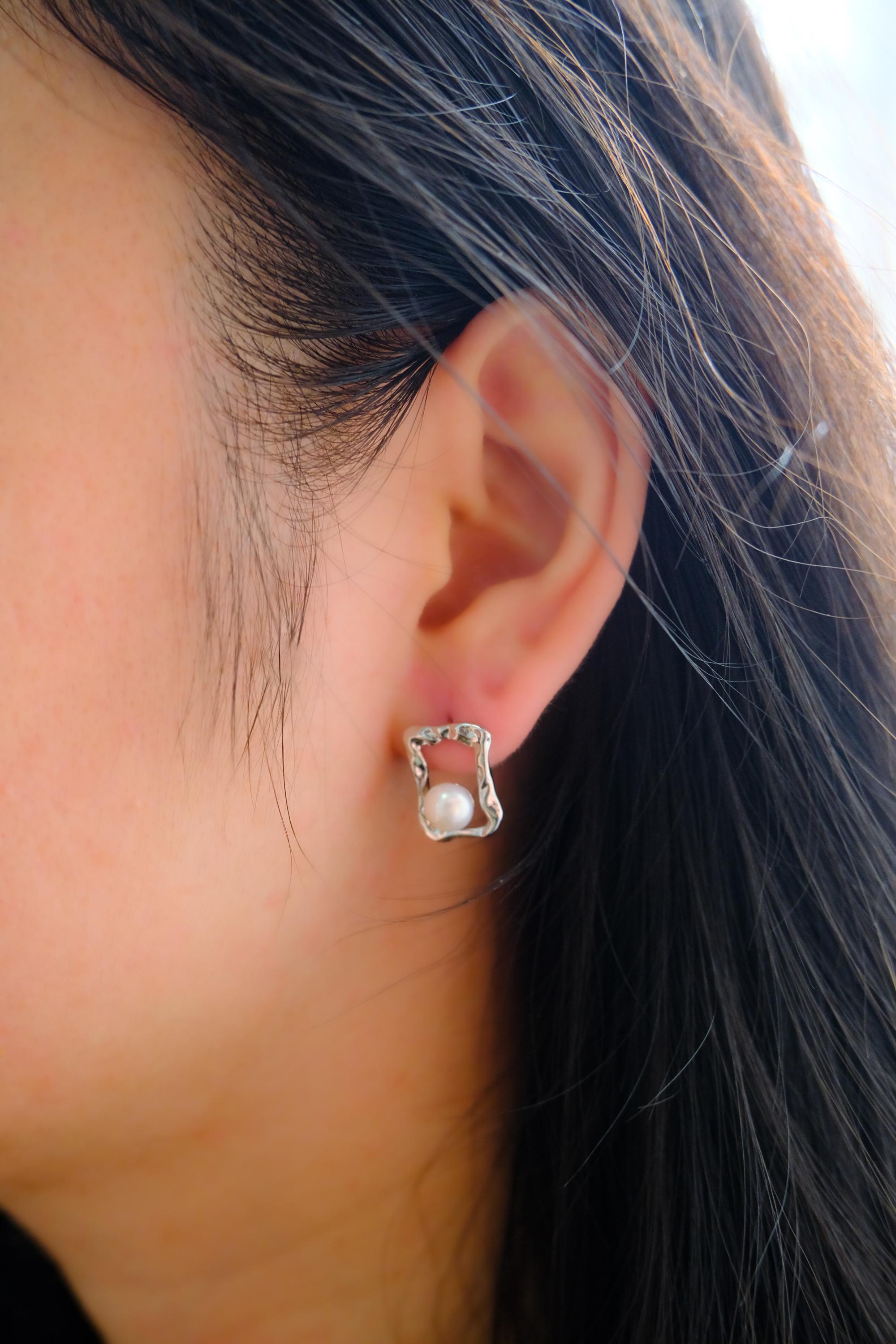 CAELLIA silver square stud earrings featuring a lustrous freshwater pearl on a person.