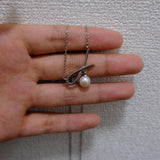 A dainty silver necklace featuring a delicate ribbon-shaped pendant with a freshwater pearl, CAELLIA.
