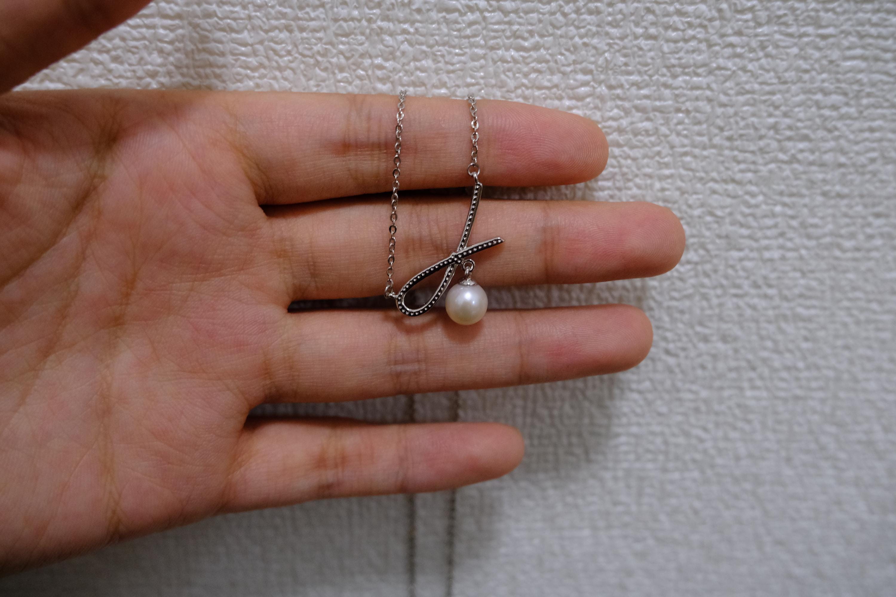 A dainty silver necklace featuring a delicate ribbon-shaped pendant with a freshwater pearl, CAELLIA.