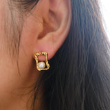 A person wears a CAELLIA gold plated stud earring featuring a freshwater pearl in a quadrate frame.