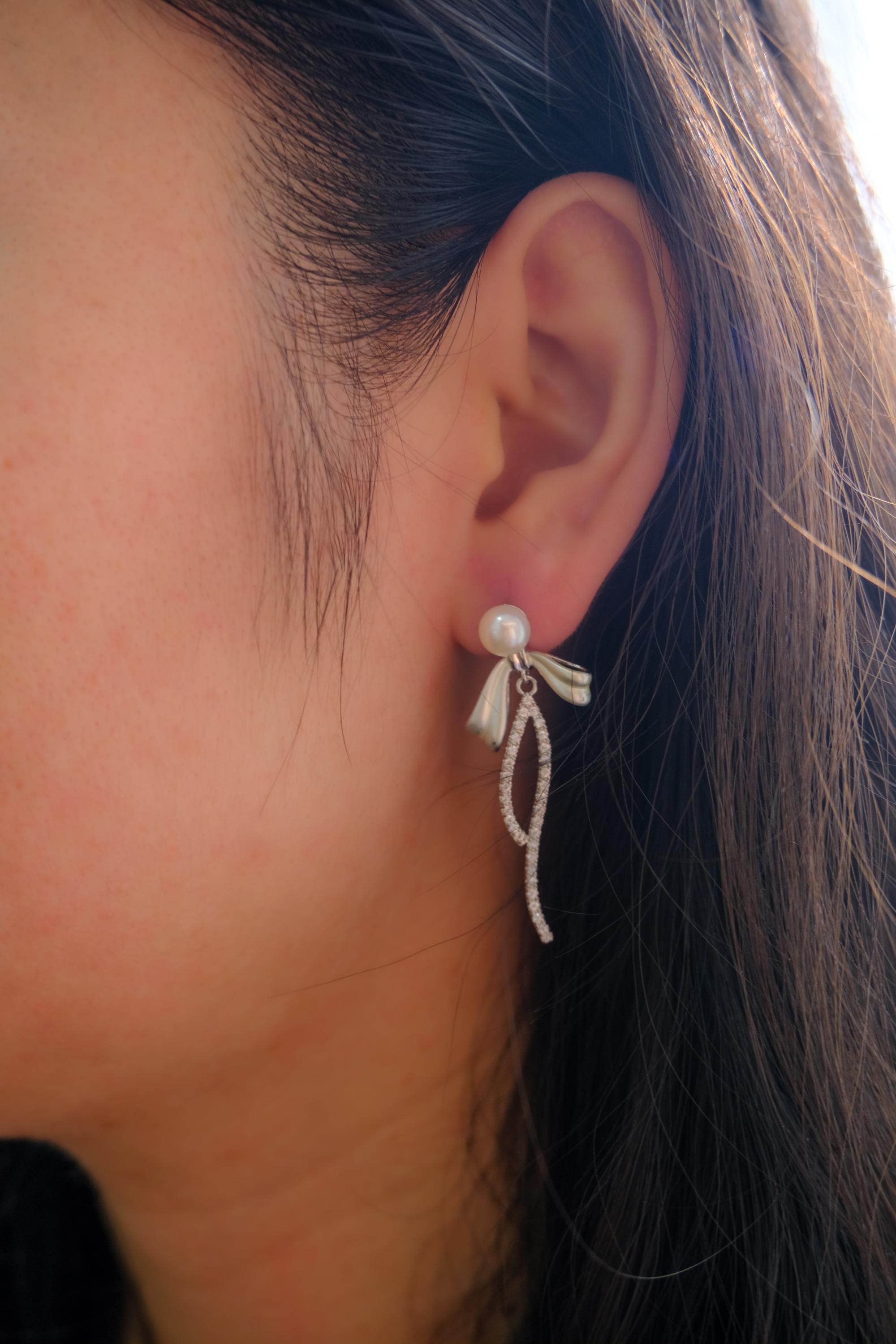 A CAELLIA pearl bow dangle earring made of 925 sterling silver worn on an earlobe.
