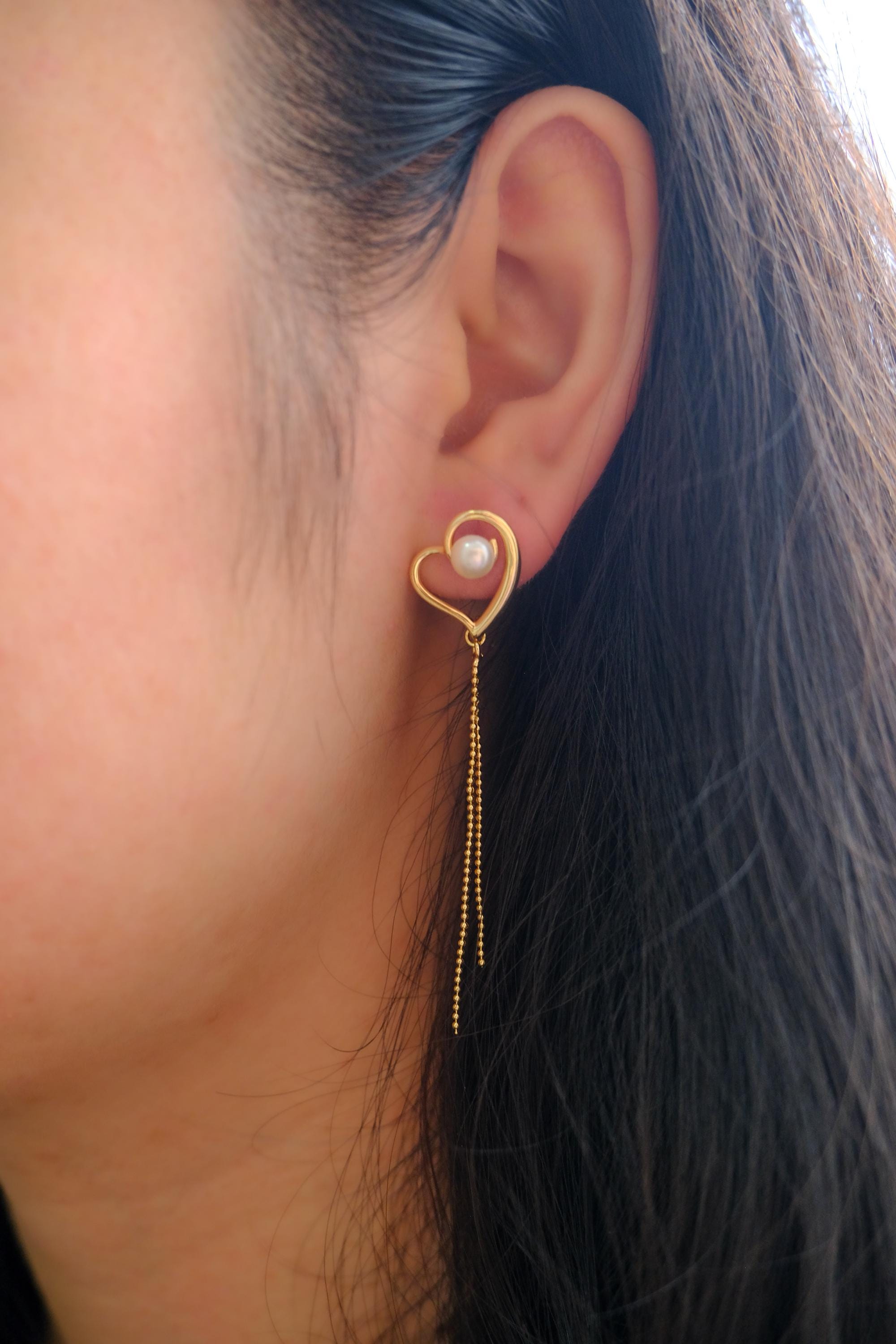 A CAELLIA heart-shaped gold earring with a central pearl and delicate dangling chains.