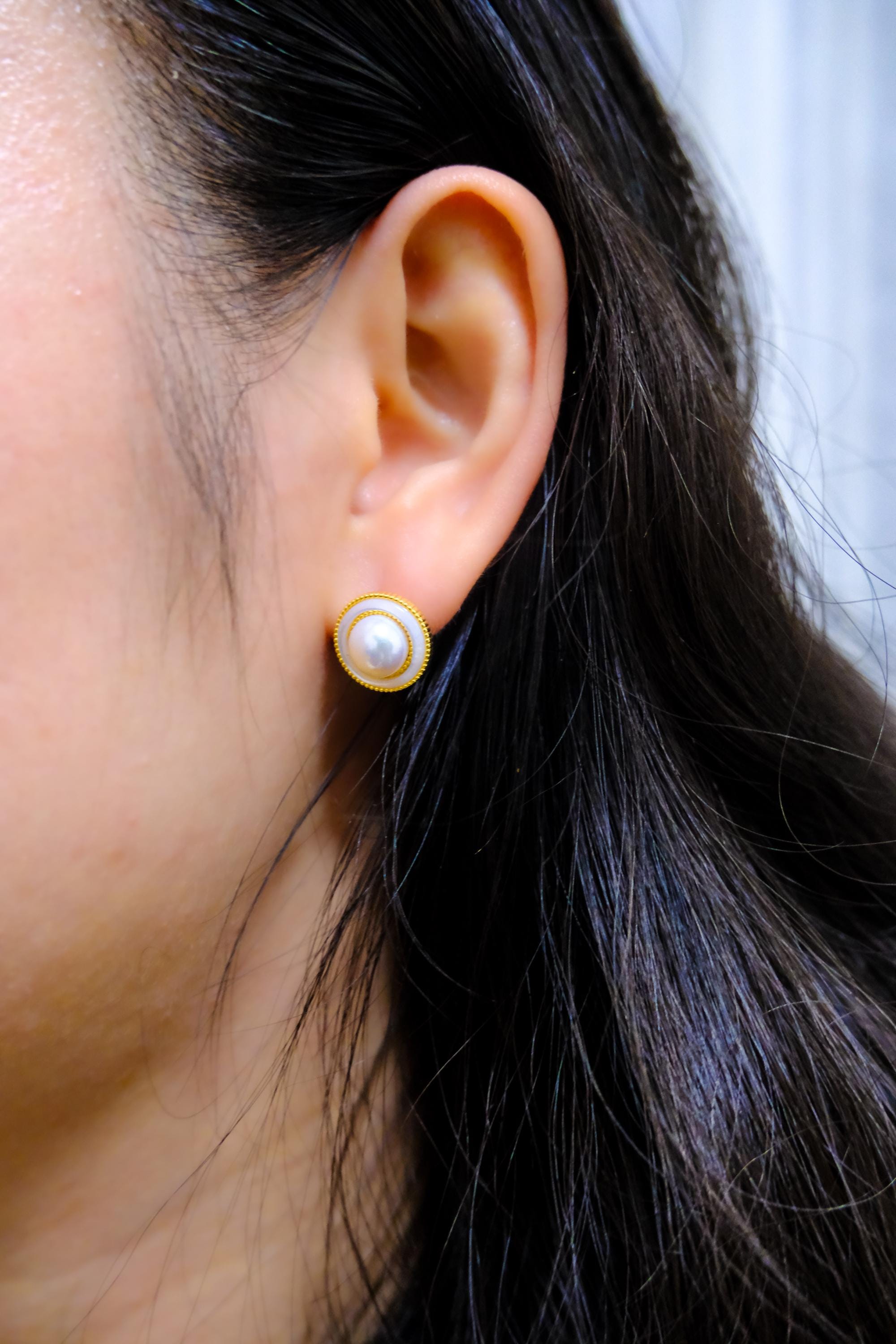 A person wears CAELLIA gold-plated freshwater pearl earrings with a minimalist circular frame.