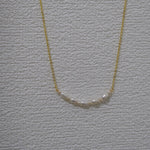 CAELLIA freshwater pearl bead necklace on a gold chain against a textured white background.
