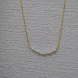 CAELLIA freshwater pearl bead necklace on a gold chain against a textured white background.
