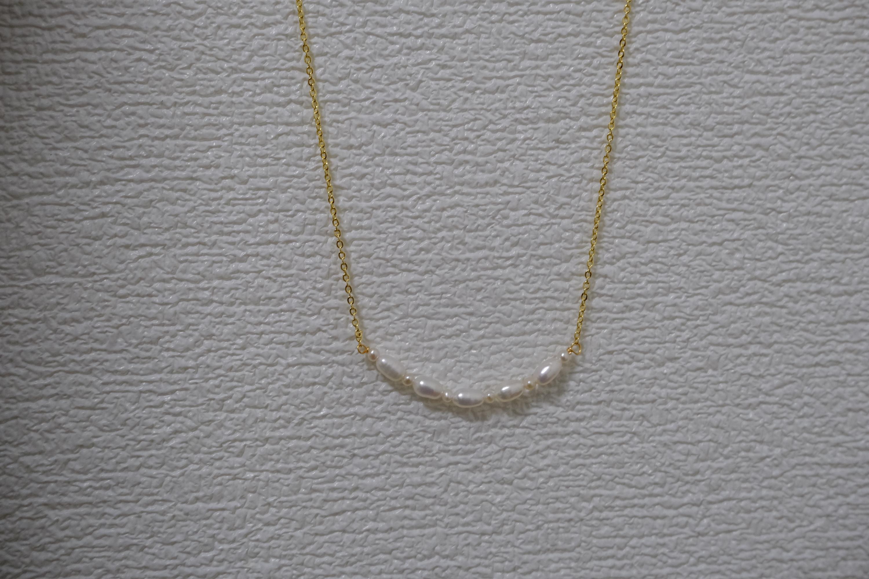 CAELLIA freshwater pearl bead necklace on a gold chain against a textured white background.