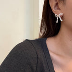 A person wearing CAELLIA butterfly bow stud earrings made of small freshwater pearls.