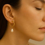 A model wears Caellia 14K gold twisted hoop earrings featuring a dangling freshwater pearl.