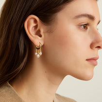 A model wears Caellia 14K gold huggie hoop earrings featuring three dangling freshwater pearls.