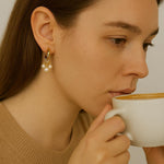 A woman wears Caellia 14K gold huggie hoop earrings featuring three small freshwater pearls.