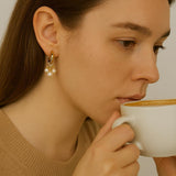 A woman wears Caellia 14K gold huggie hoop earrings featuring three small freshwater pearls.