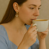 A woman wears Caellia 14K gold huggie hoop earrings featuring delicate freshwater pearl charms.