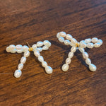 CAELLIA butterfly bow stud earrings handcrafted with small freshwater pearls on a wooden surface.