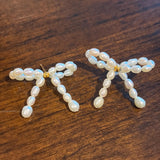 CAELLIA butterfly bow stud earrings handcrafted with small freshwater pearls on a wooden surface.