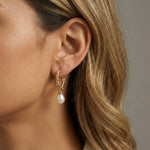 A close-up of a woman wearing Caellia 14K gold twisted hoop earrings with a freshwater pearl drop.