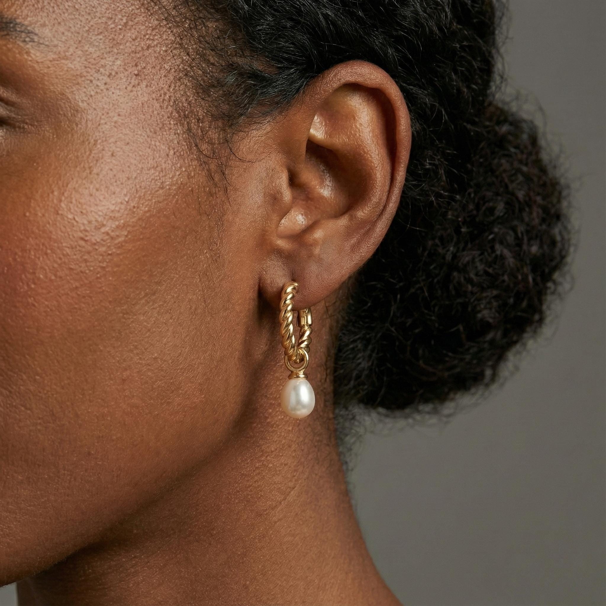 A model wears Caellia 14K gold twisted hoop earrings featuring a dangling freshwater pearl.