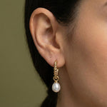 A close-up of a Caellia 14K gold twisted hoop earring with a dangling freshwater pearl.