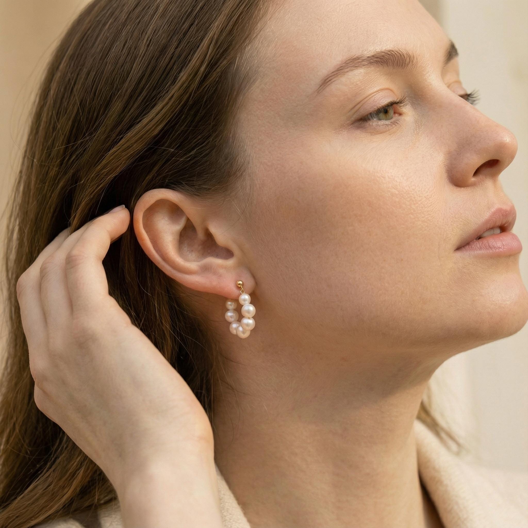 A model wears Caellia 18K gold hoop earrings featuring a circular arrangement of freshwater pearls.