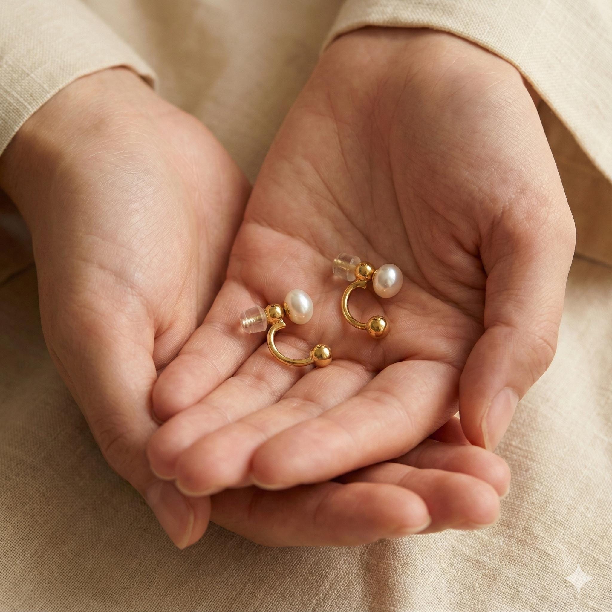 Caellia 14K gold double-sided stud earrings featuring freshwater pearls held in cupped hands.