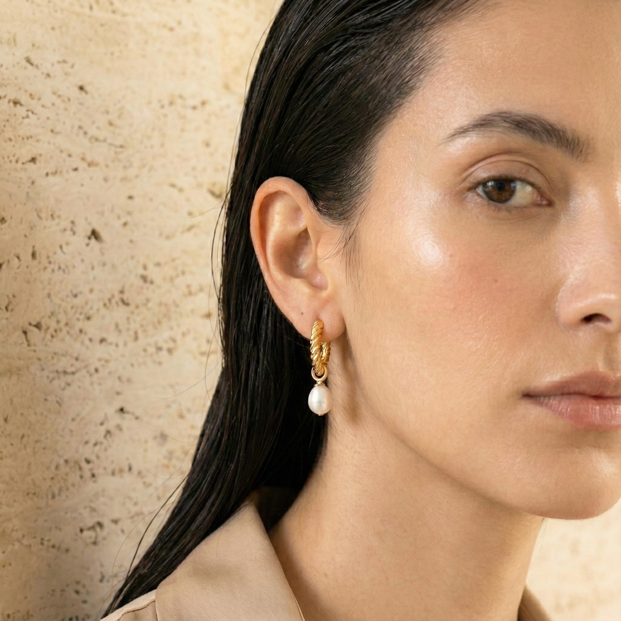 A model wears Caellia 14K gold twisted hoop earrings featuring a dangling freshwater pearl.
