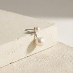Caellia sterling silver double freshwater pearl stud earrings resting on a textured surface.