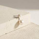 Caellia sterling silver double freshwater pearl stud earrings resting on a textured surface.