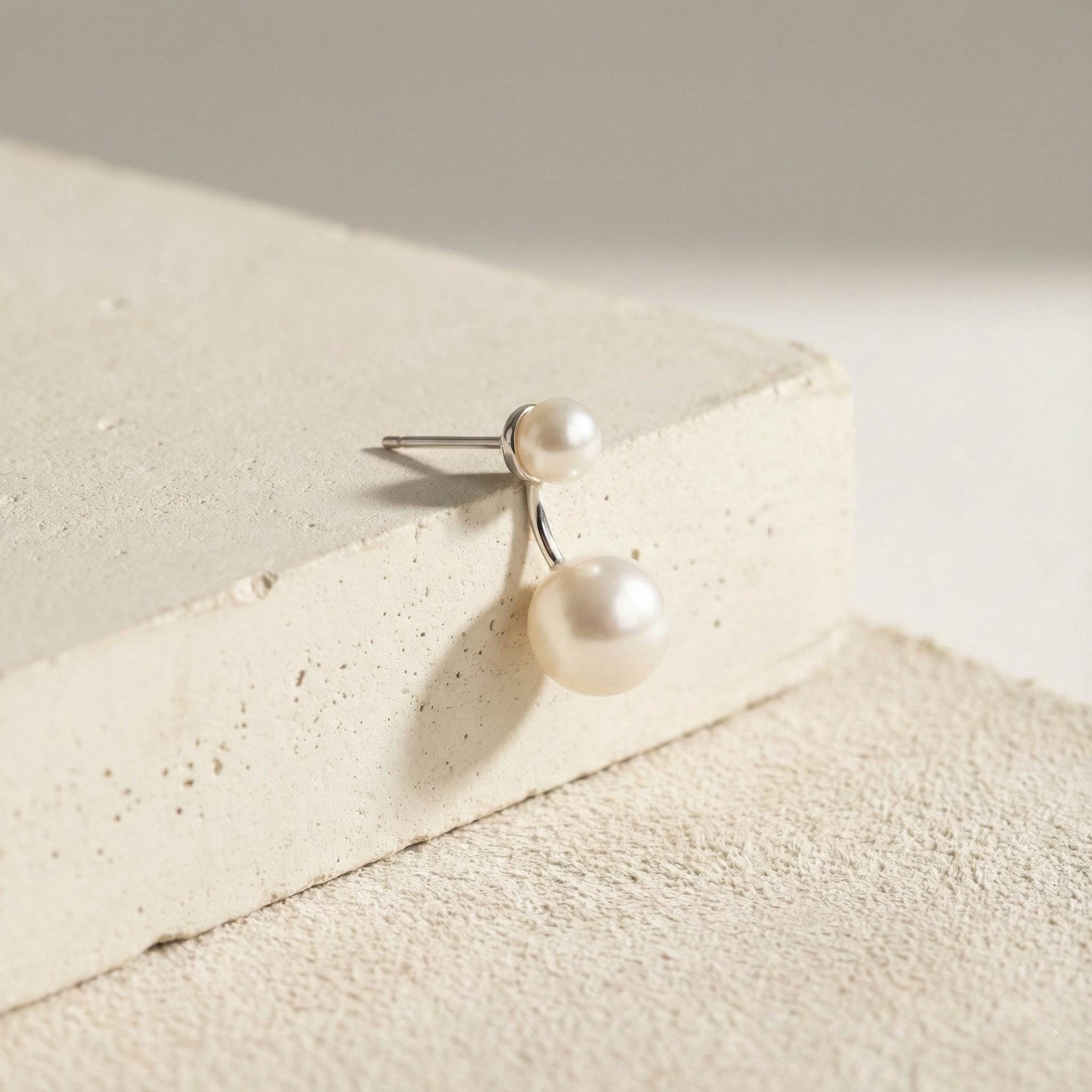 Caellia sterling silver double freshwater pearl stud earrings resting on a textured surface.