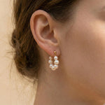 A model wears Caellia 18K gold hoop earrings featuring a cluster of lustrous freshwater pearls.