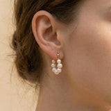 A model wears Caellia 18K gold hoop earrings featuring a cluster of lustrous freshwater pearls.