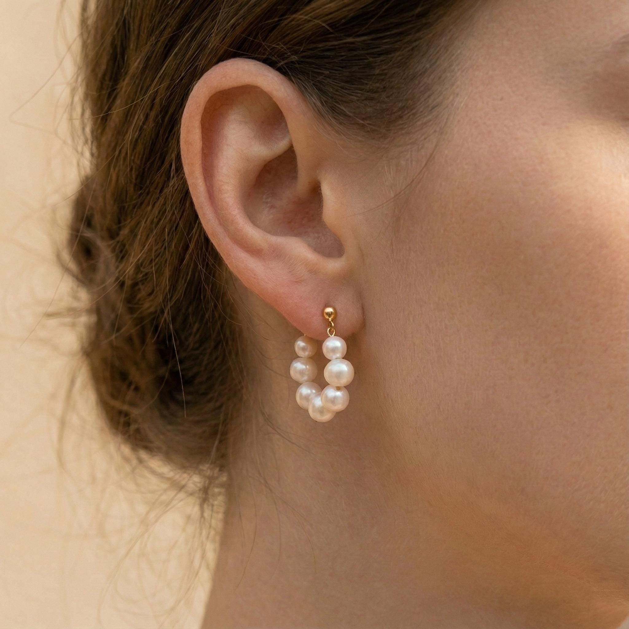 A model wears Caellia 18K gold hoop earrings featuring a cluster of lustrous freshwater pearls.