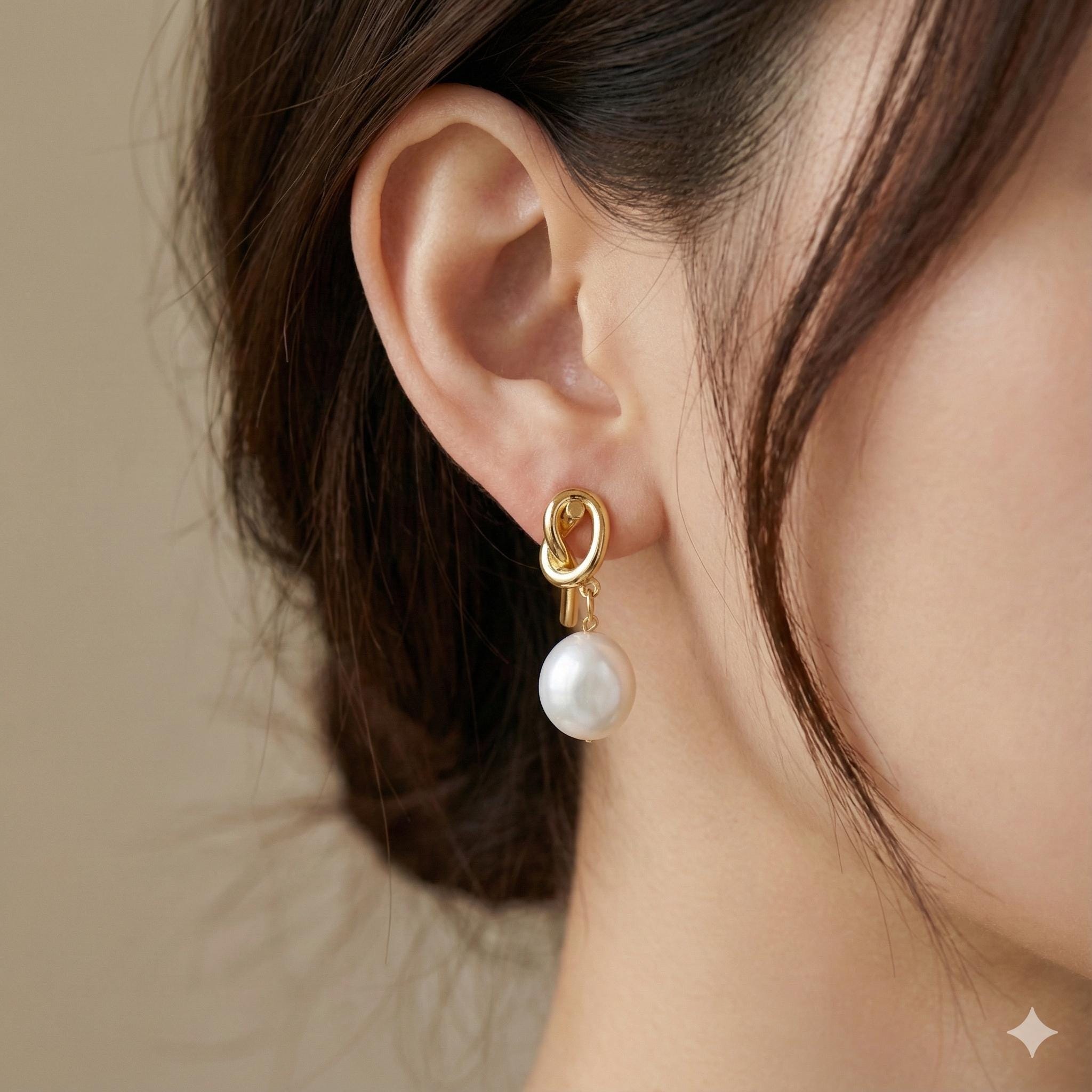 A close-up of a Caellia 14K gold knot earring featuring a dangling freshwater pearl.