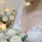 A bride wears a dainty CAELLIA freshwater pearl pendant necklace with a delicate bow design.