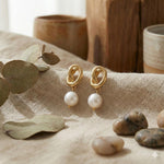 Caellia 14K gold knot earrings featuring dangling freshwater pearls on a textured fabric surface.