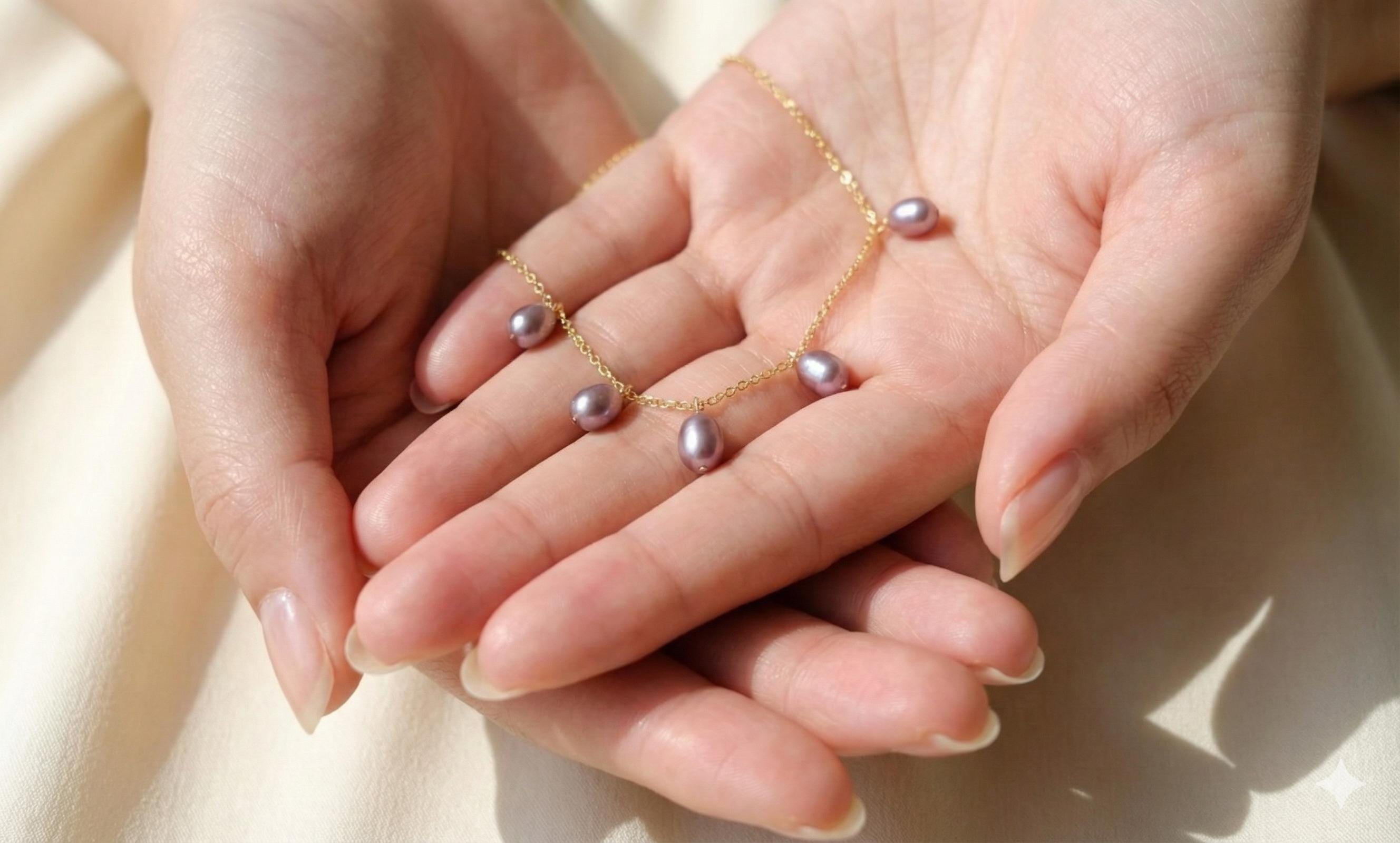 A dainty CAELLIA lavender freshwater pearl choker on a 14K gold plated chain held in two hands.