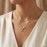 CAELLIA gold layered necklace featuring a pave letter K pendant and a single pearl accent.
