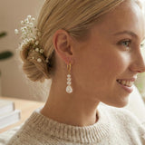A woman wearing Caellia 14K gold hoop earrings with three dangling baroque freshwater pearls.