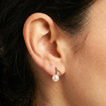 A close-up of a Caellia 14K gold music note earring featuring a freshwater pearl on an earlobe.