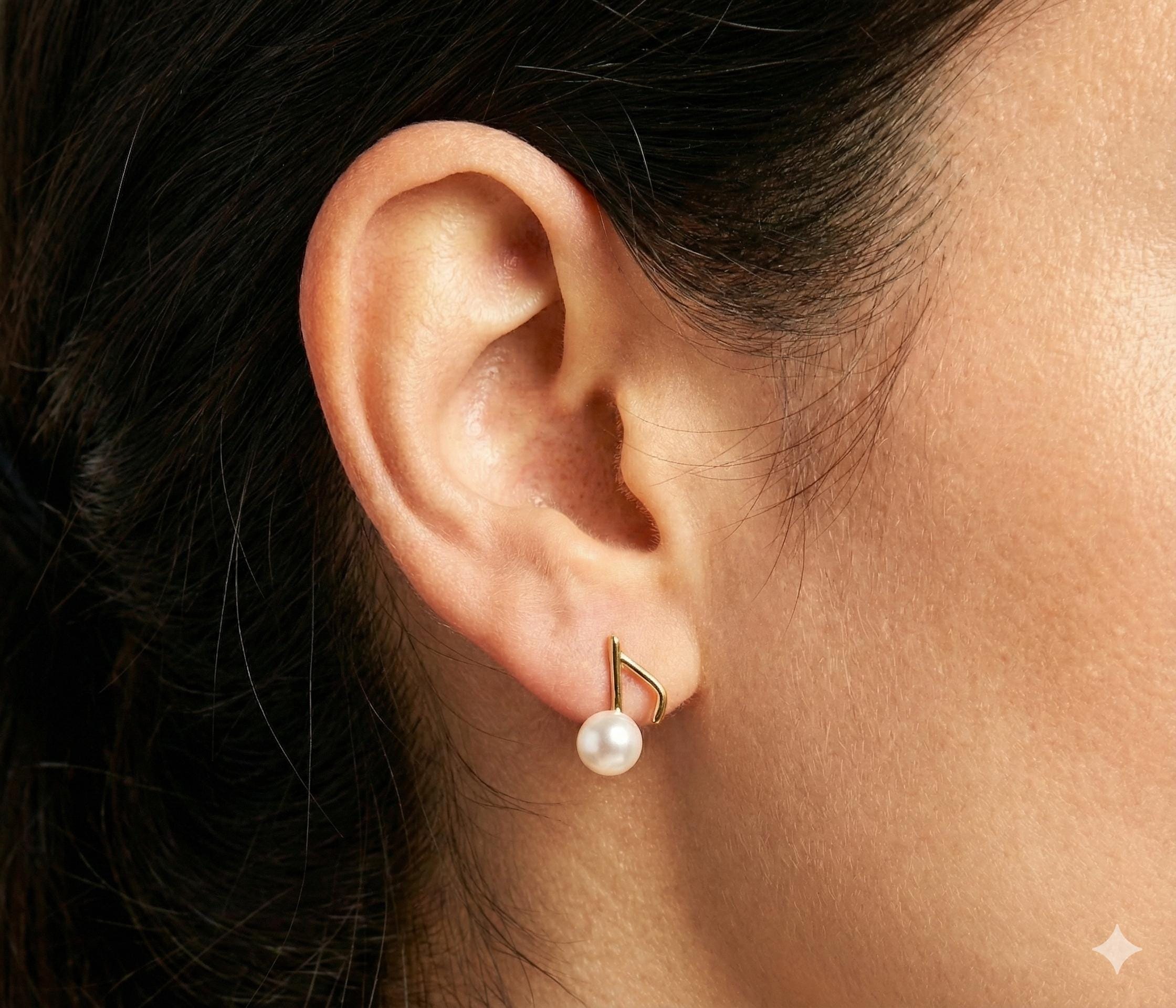 A close-up of a Caellia 14K gold music note earring featuring a freshwater pearl on an earlobe.