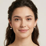 A woman wears Caellia 14K gold music note asymmetrical earrings featuring freshwater pearls.