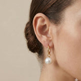 A model wears Caellia 18K gold hoop earrings featuring a dangling freshwater pearl.
