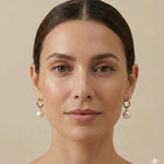 A model wearing Caellia 18K gold hoop earrings featuring a dangling freshwater pearl.