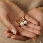 A pair of Caellia 18K gold hoop earrings featuring lustrous freshwater pearls held in cupped hands.