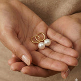A pair of Caellia 18K gold hoop earrings featuring lustrous freshwater pearls held in cupped hands.