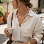 A woman wearing a Caellia 14K gold and freshwater pearl necklace while holding a coffee cup.