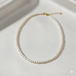 Caellia 14K gold and freshwater pearl choker necklace on a white silk background.