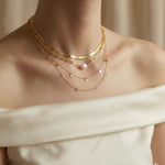 A model wearing a layered Caellia 18K gold necklace set featuring a baroque pearl and coin charms.